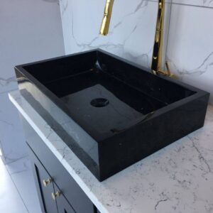 Black marble sink on white marble countertop with gold faucet.