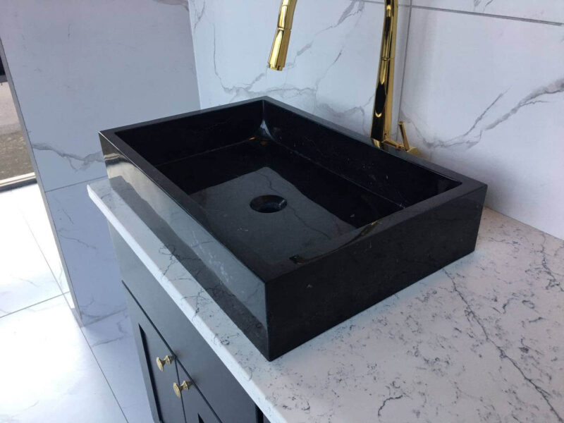 Black marble sink on white marble countertop with gold faucet.