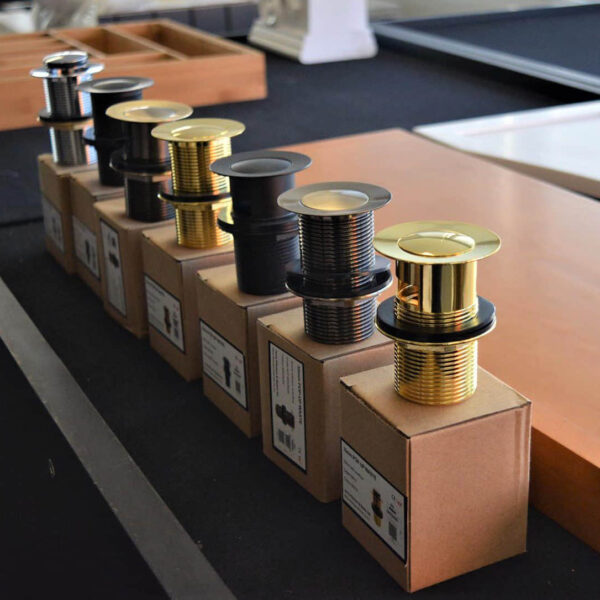 Pop-up wastes in various finishes displayed on boxes.