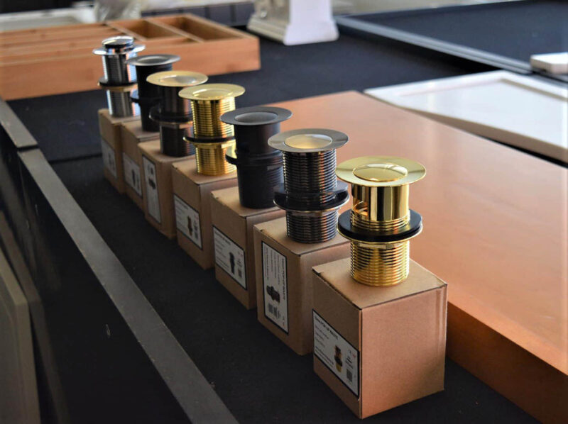 Pop-up wastes in various finishes displayed on boxes.