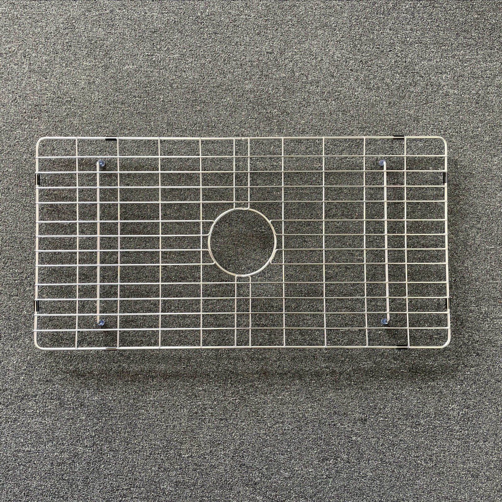 Stainless steel sink grid on a textured surface.