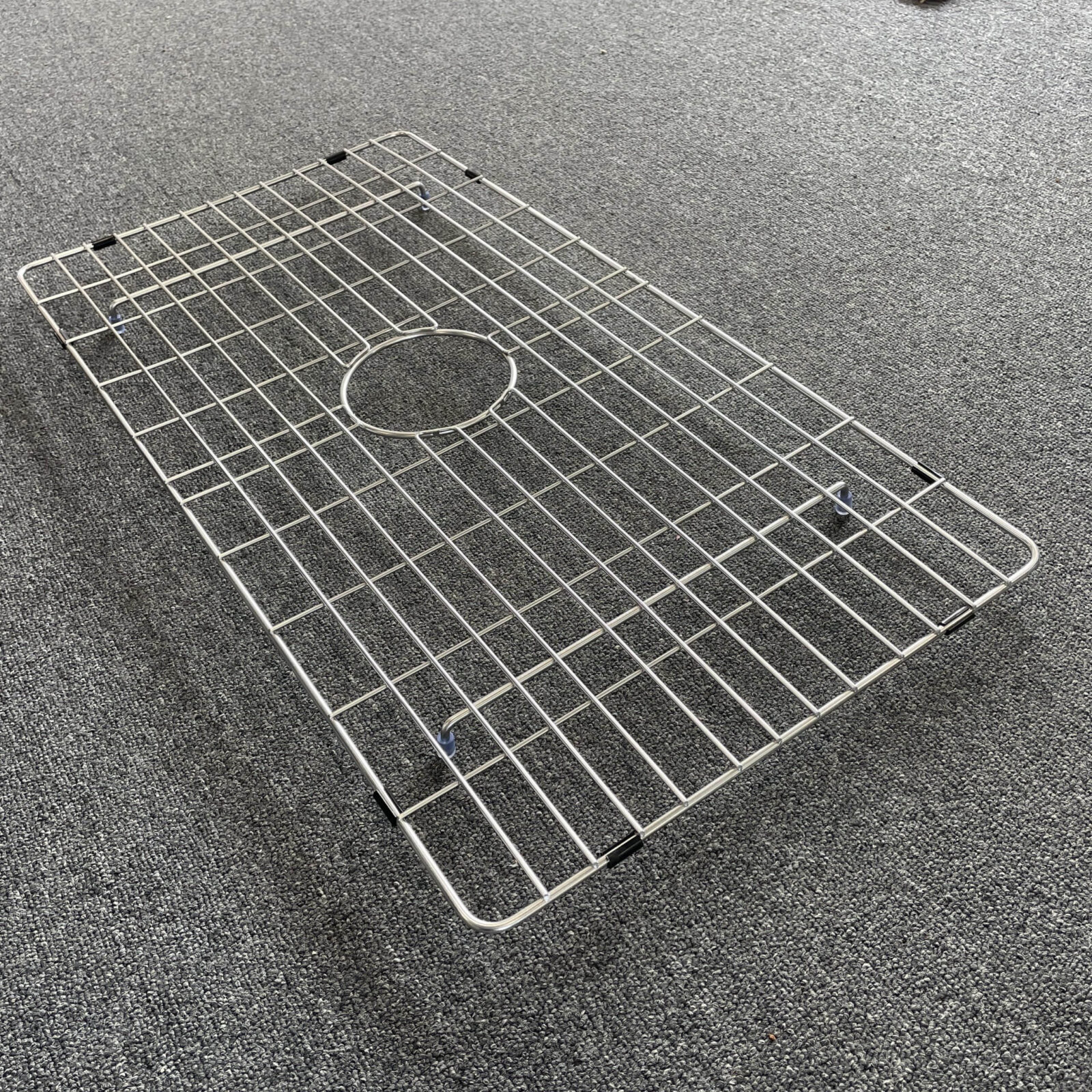 Stainless steel sink grid on gray carpet.