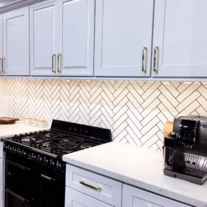 Modern kitchen with white cabinets, herringbone backsplash, and espresso machine.