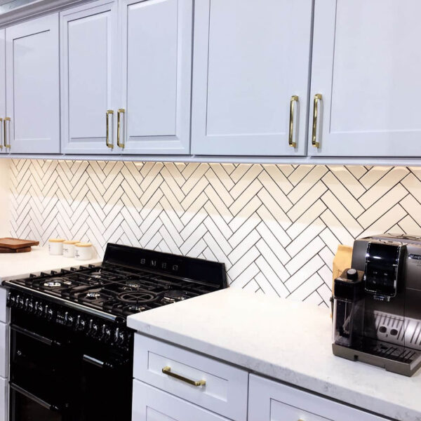 Modern kitchen with white cabinets, herringbone backsplash, and espresso machine.
