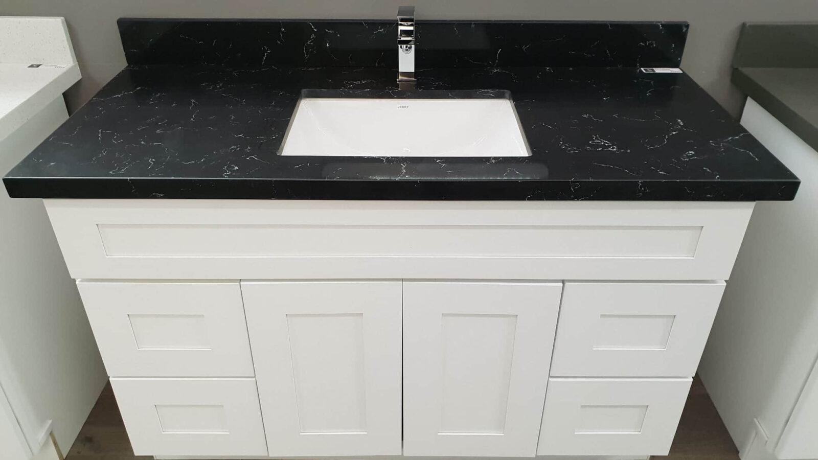 White bathroom vanity with black countertop and sink.