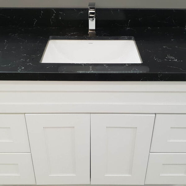 White bathroom vanity with black countertop and sink.