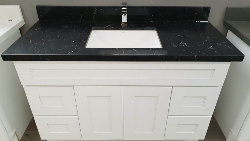 White bathroom vanity with black countertop and sink.