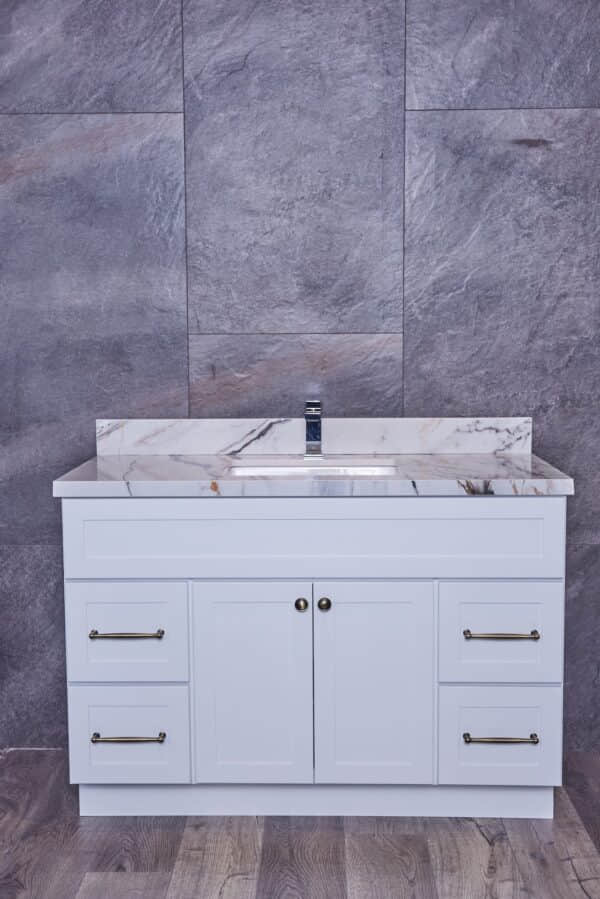 White bathroom vanity with marble countertop against gray stone wall.
