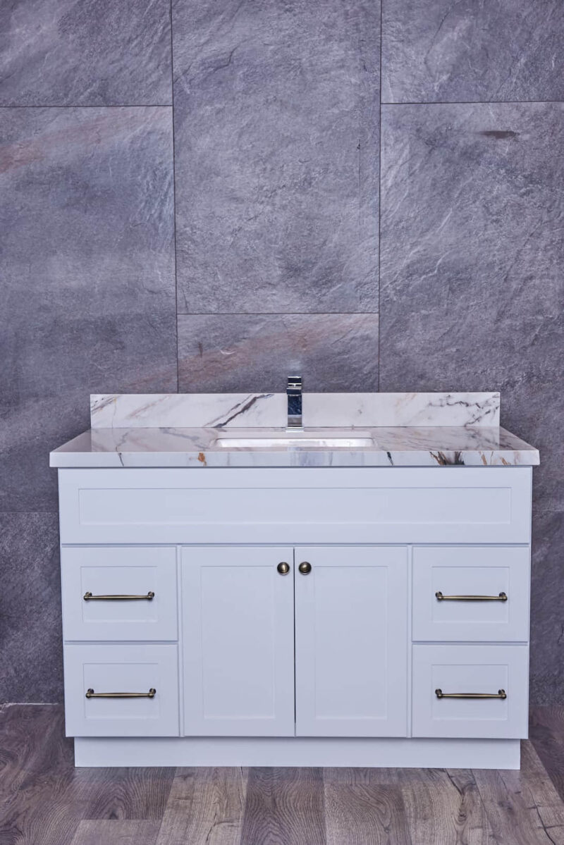 White bathroom vanity with marble countertop against gray stone wall.