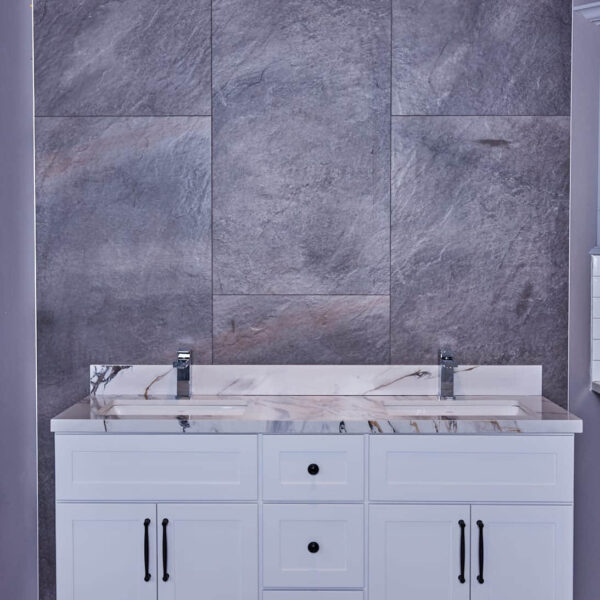 White bathroom vanity with marble countertop against gray stone wall.