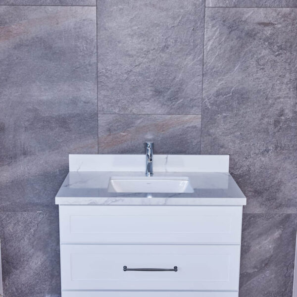 White bathroom vanity with sink against gray tiled wall.