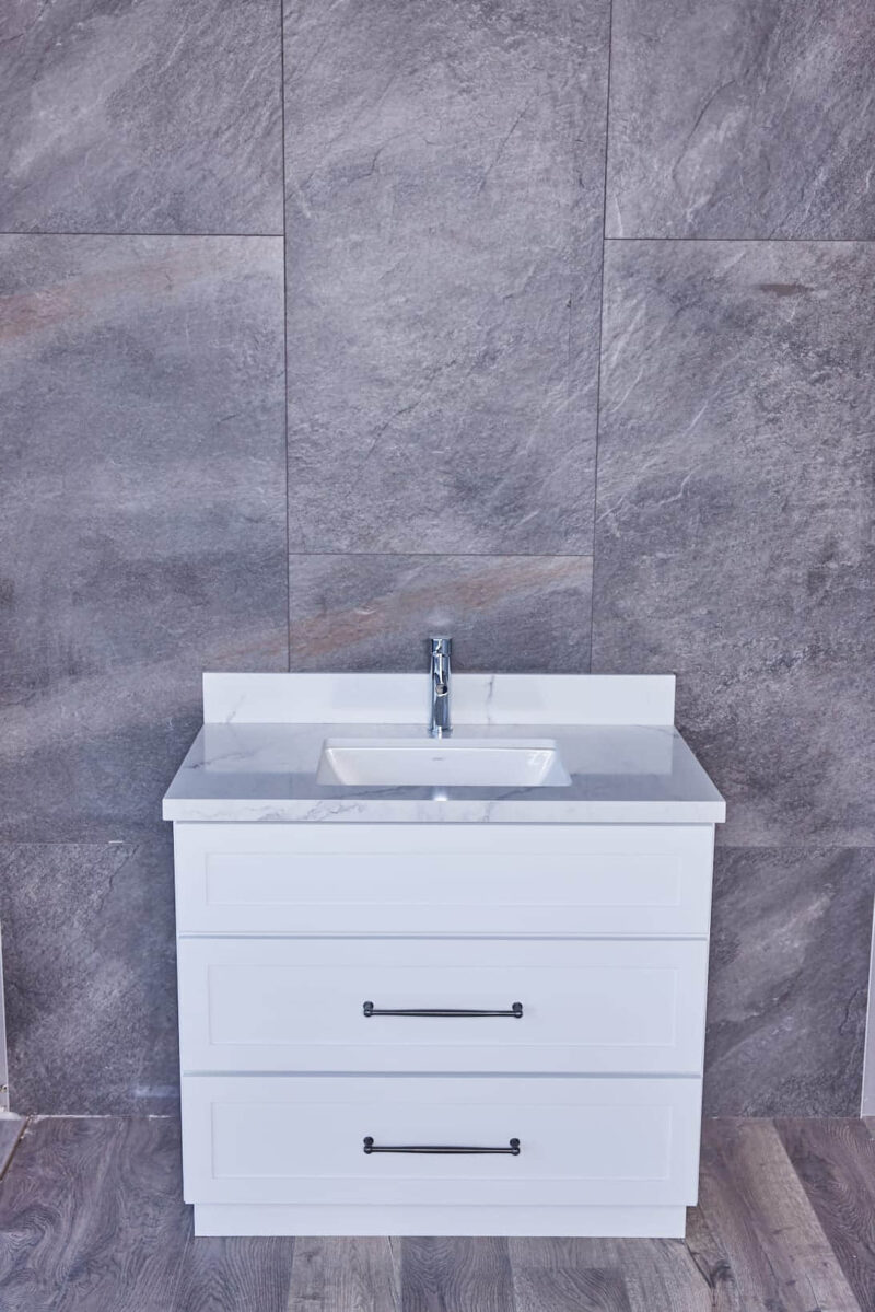 White bathroom vanity with sink against gray tiled wall.