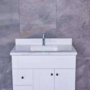 White bathroom vanity with marble countertop and modern faucet against gray tiled wall.