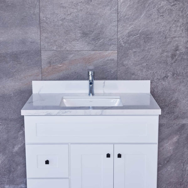 White bathroom vanity with marble countertop and modern faucet against gray tiled wall.