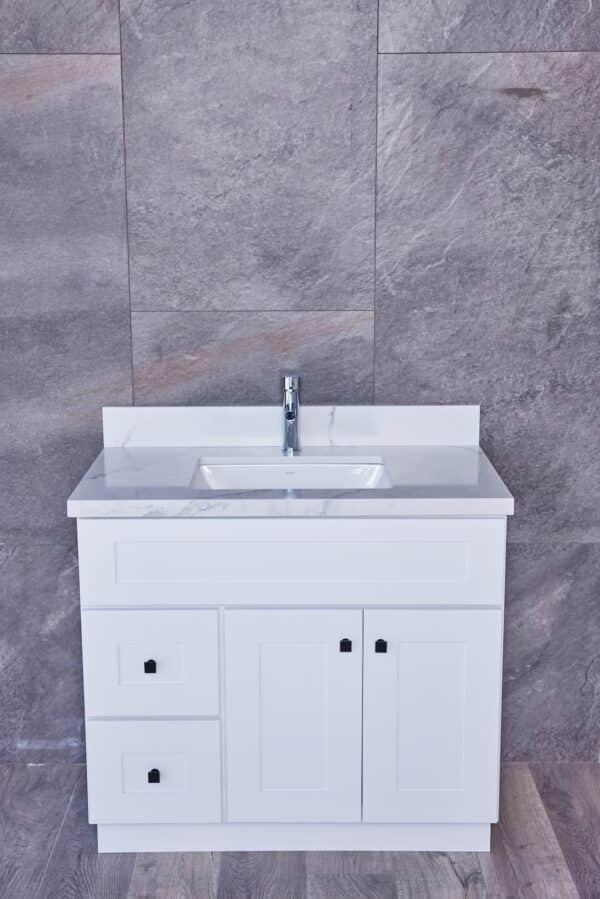 White bathroom vanity with marble countertop and modern faucet against gray tiled wall.