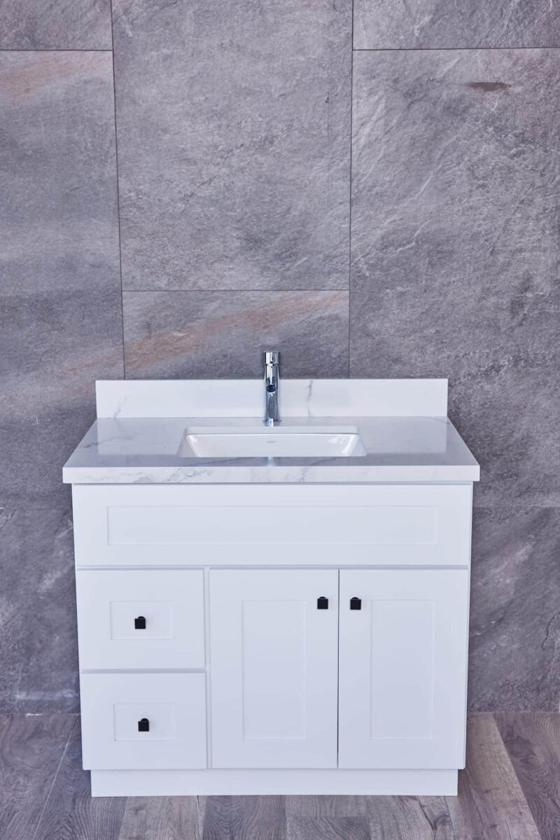 White bathroom vanity with marble countertop and modern faucet against gray tiled wall.