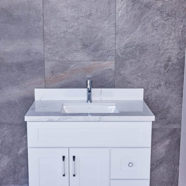 White bathroom vanity with marble countertop against gray stone wall.