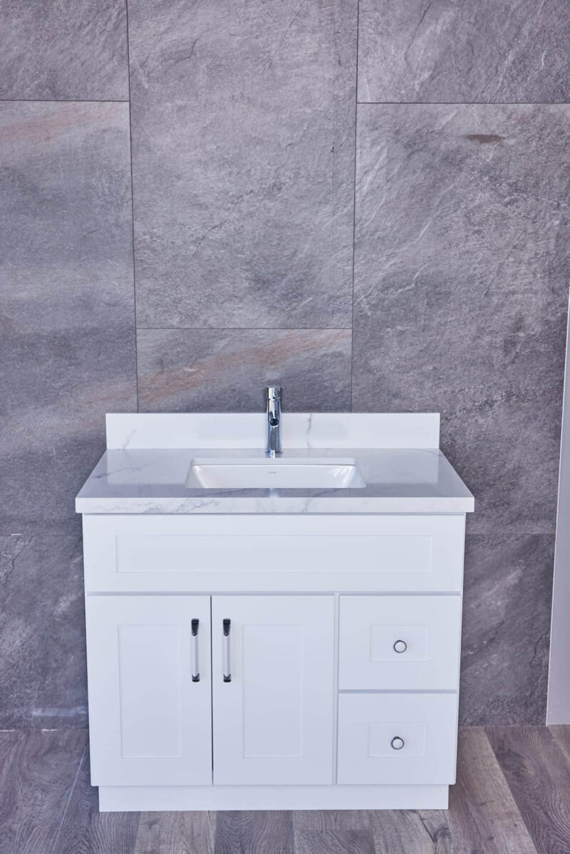 White bathroom vanity with marble countertop against gray stone wall.