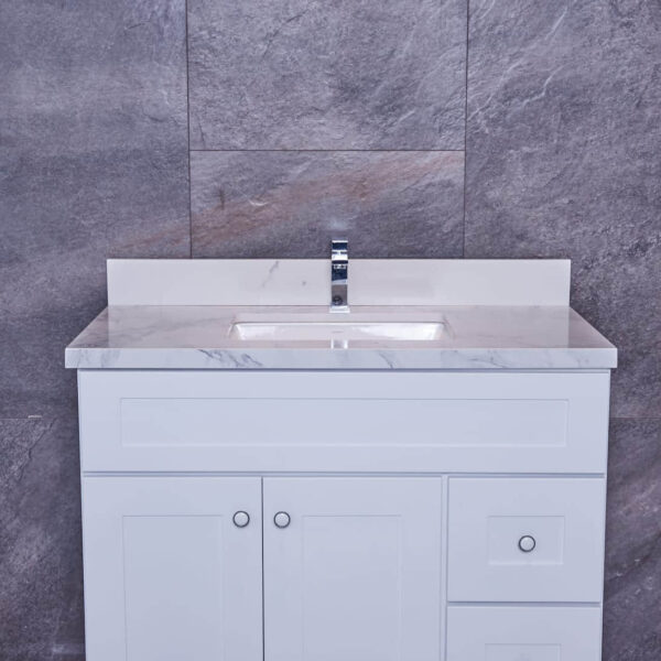 White bathroom vanity with marble countertop against gray stone wall.