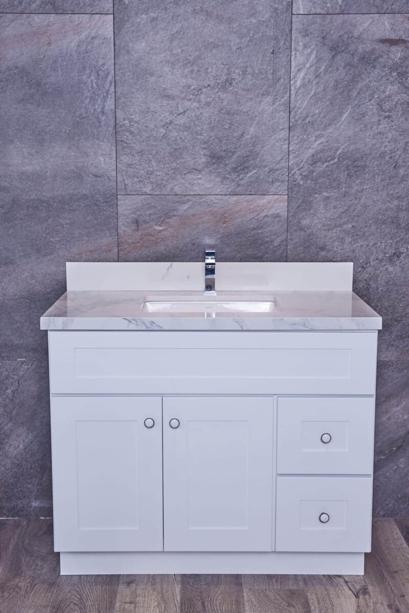 White bathroom vanity with marble countertop against gray stone wall.