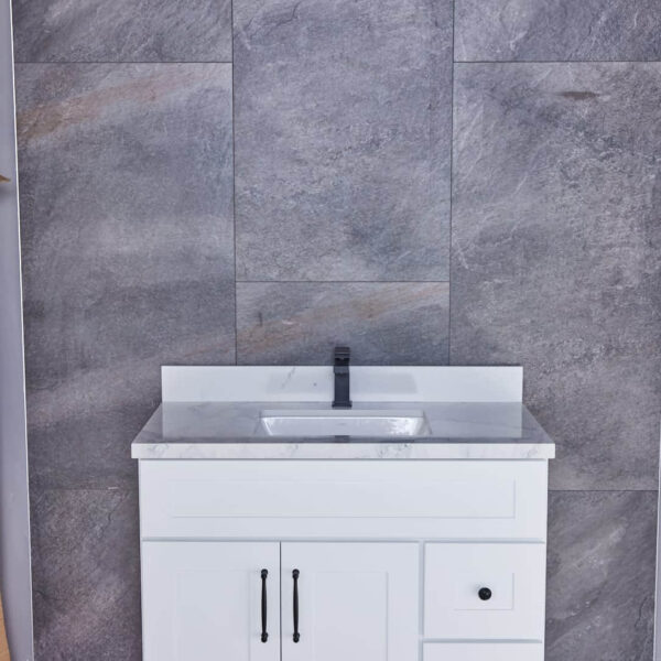 White bathroom vanity with marble countertop against gray tiled wall.