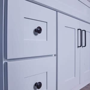 White kitchen cabinet with black handles and knobs on wooden floor.