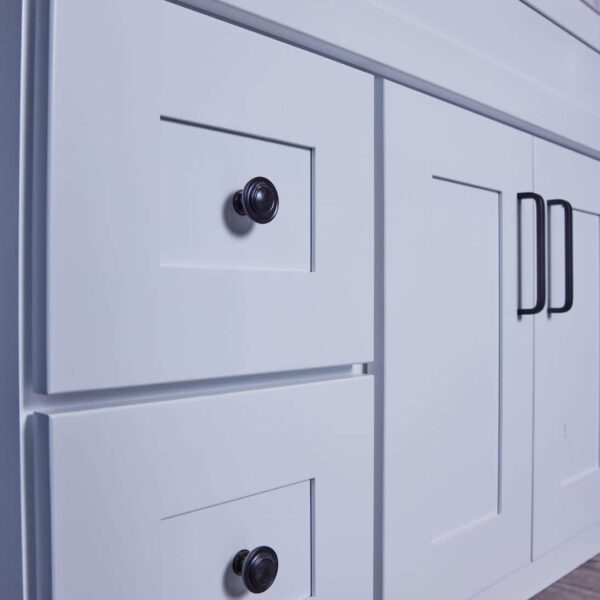 White kitchen cabinet with black handles and knobs on wooden floor.
