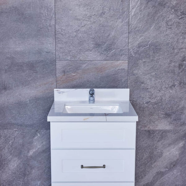 White bathroom vanity with sink against gray tiled wall.