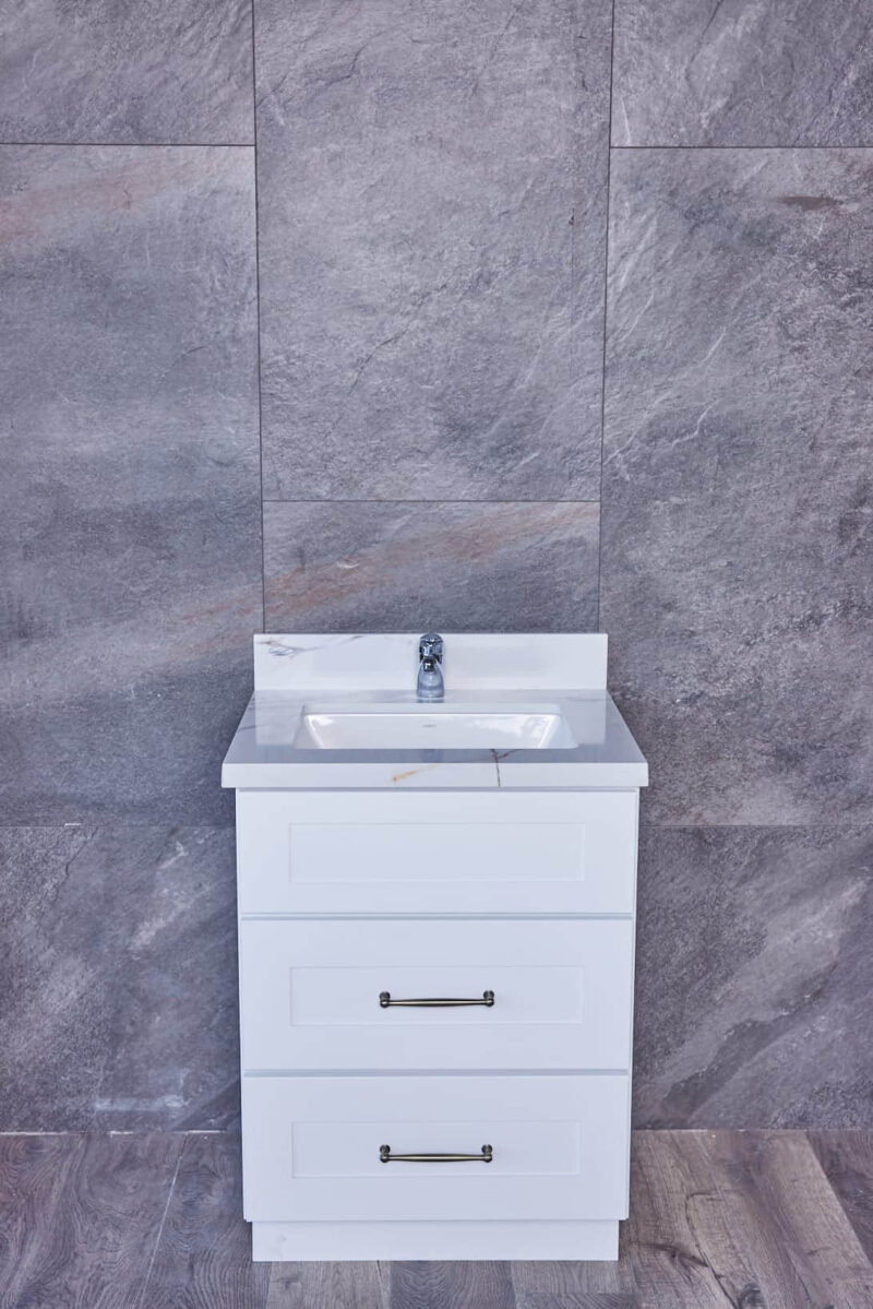 White bathroom vanity with sink against gray tiled wall.