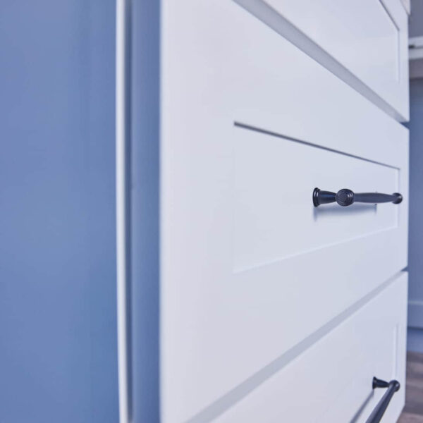 White kitchen drawers with black handles against a blue wall.