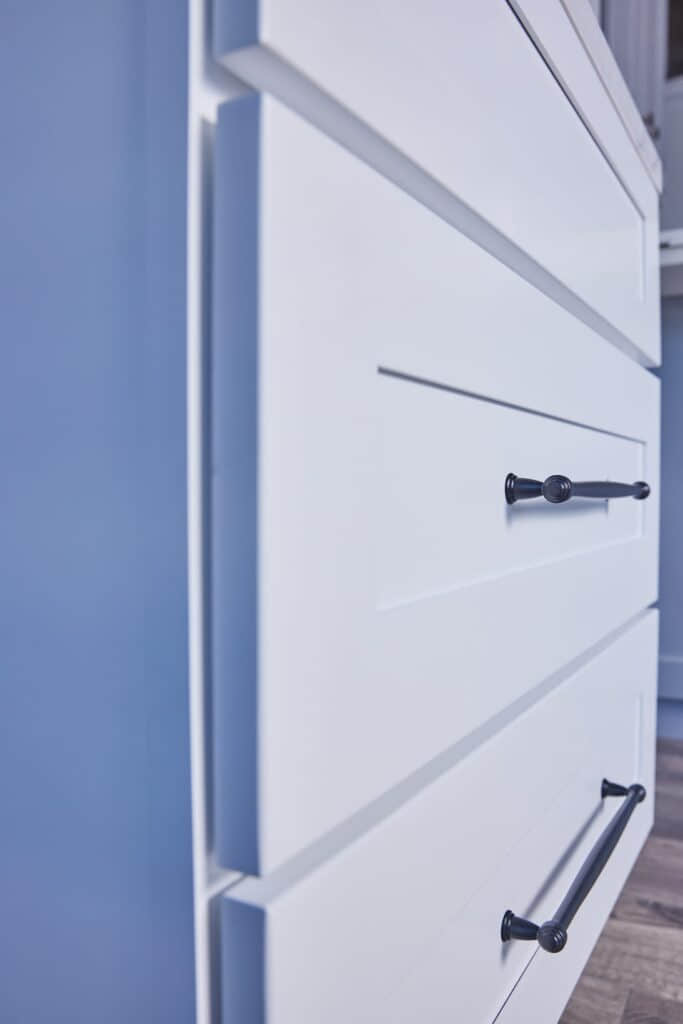 White kitchen drawers with black handles against a blue wall.