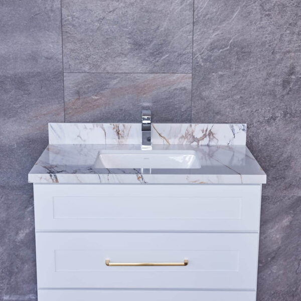 White bathroom vanity with marble countertop and gold handles against gray tiled wall.