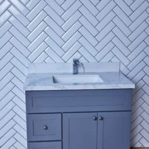 Blue bathroom vanity with marble countertop and herringbone tile backsplash.