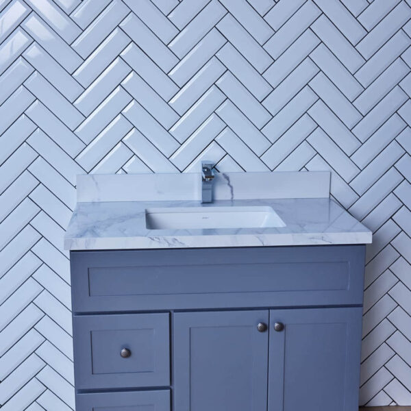 Blue bathroom vanity with marble countertop and herringbone tile backsplash.