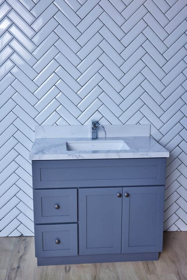 Blue bathroom vanity with marble countertop and herringbone tile backsplash.