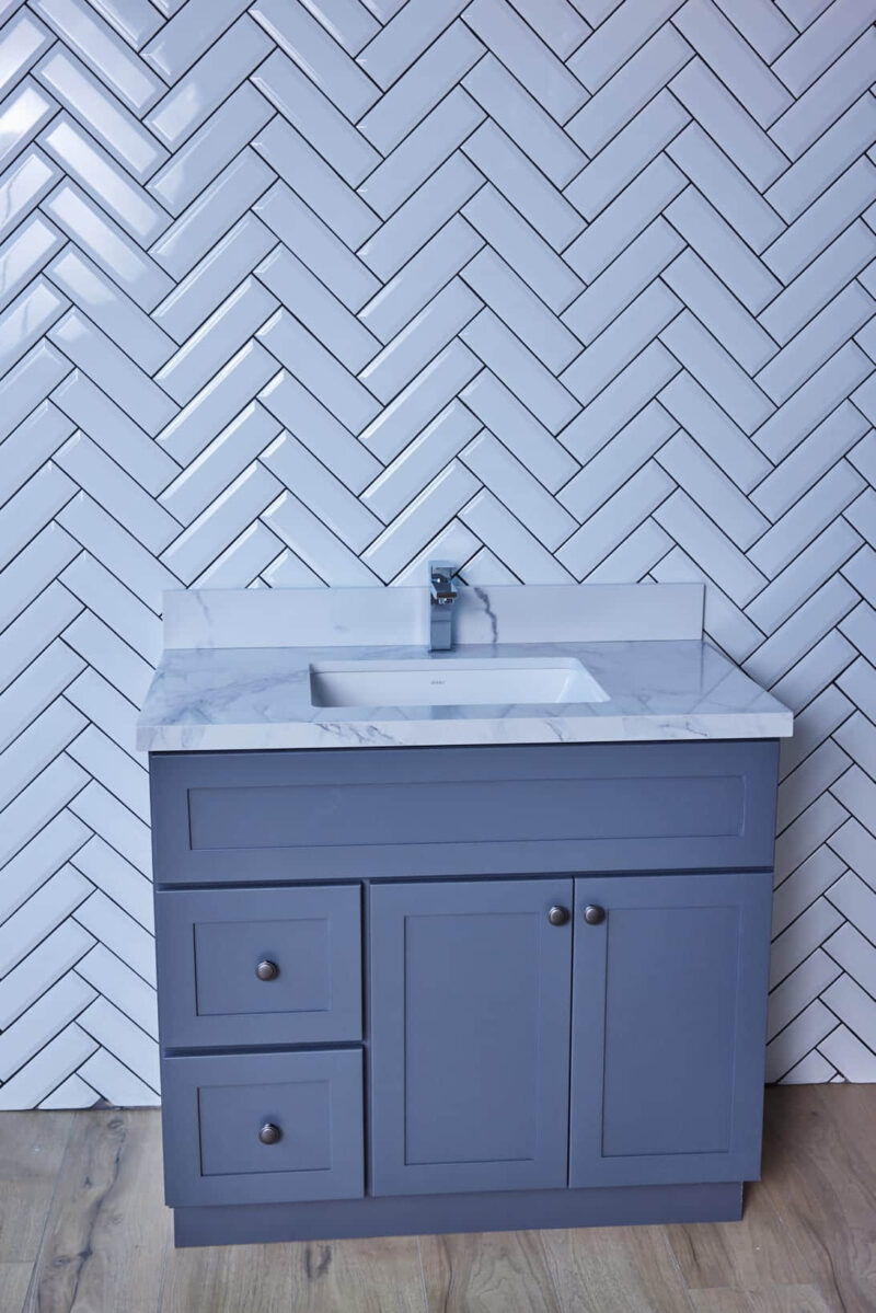 Blue bathroom vanity with marble countertop and herringbone tile backsplash.