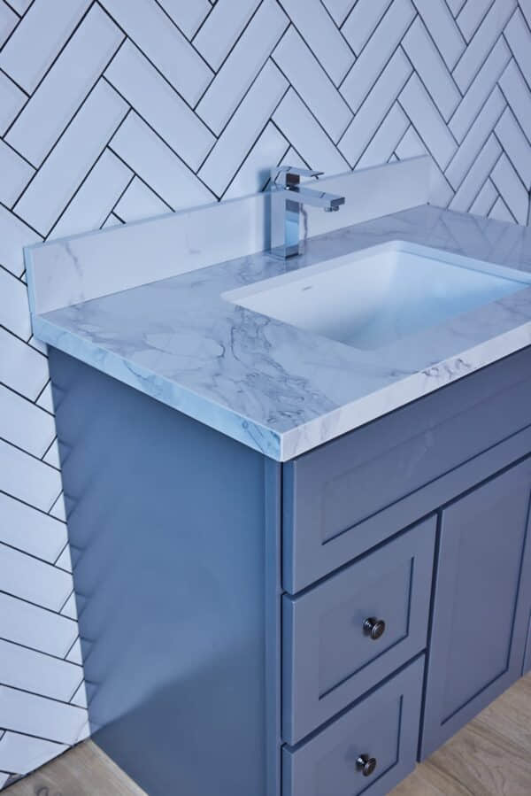 Marble countertop with sink and blue cabinet against herringbone tile wall.