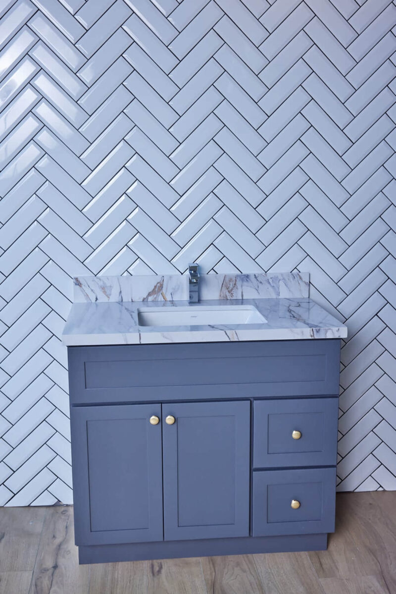 Blue bathroom vanity with marble countertop and herringbone tile wall.