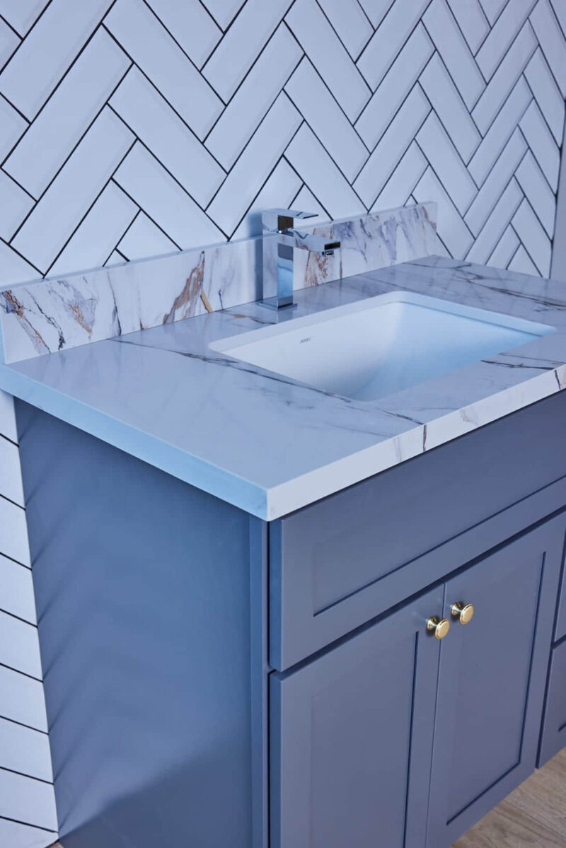 Modern bathroom sink with marble countertop and blue cabinet.