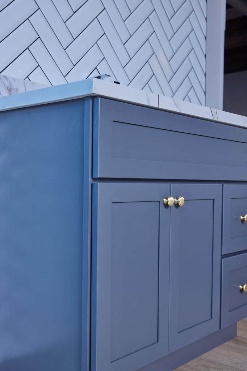 Blue kitchen cabinet with gold knobs and marble countertop.