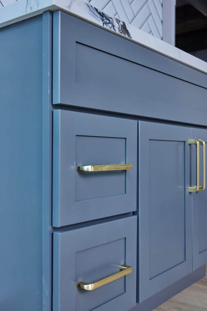 Blue kitchen cabinet with gold handles and marble countertop.