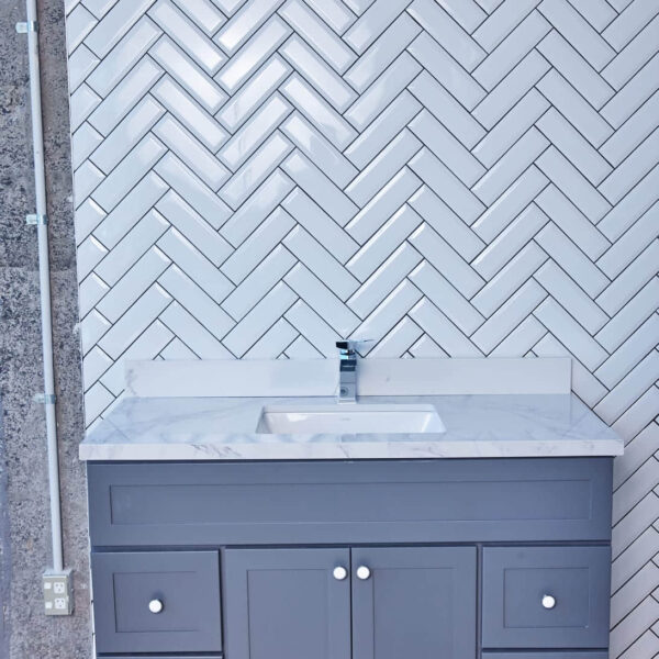 Gray bathroom vanity with marble countertop and herringbone tile backsplash.