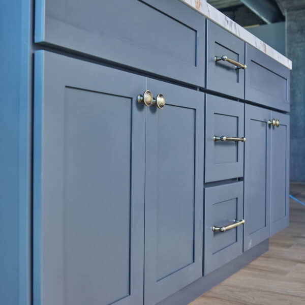 Blue kitchen cabinets with brass handles on wooden floor.