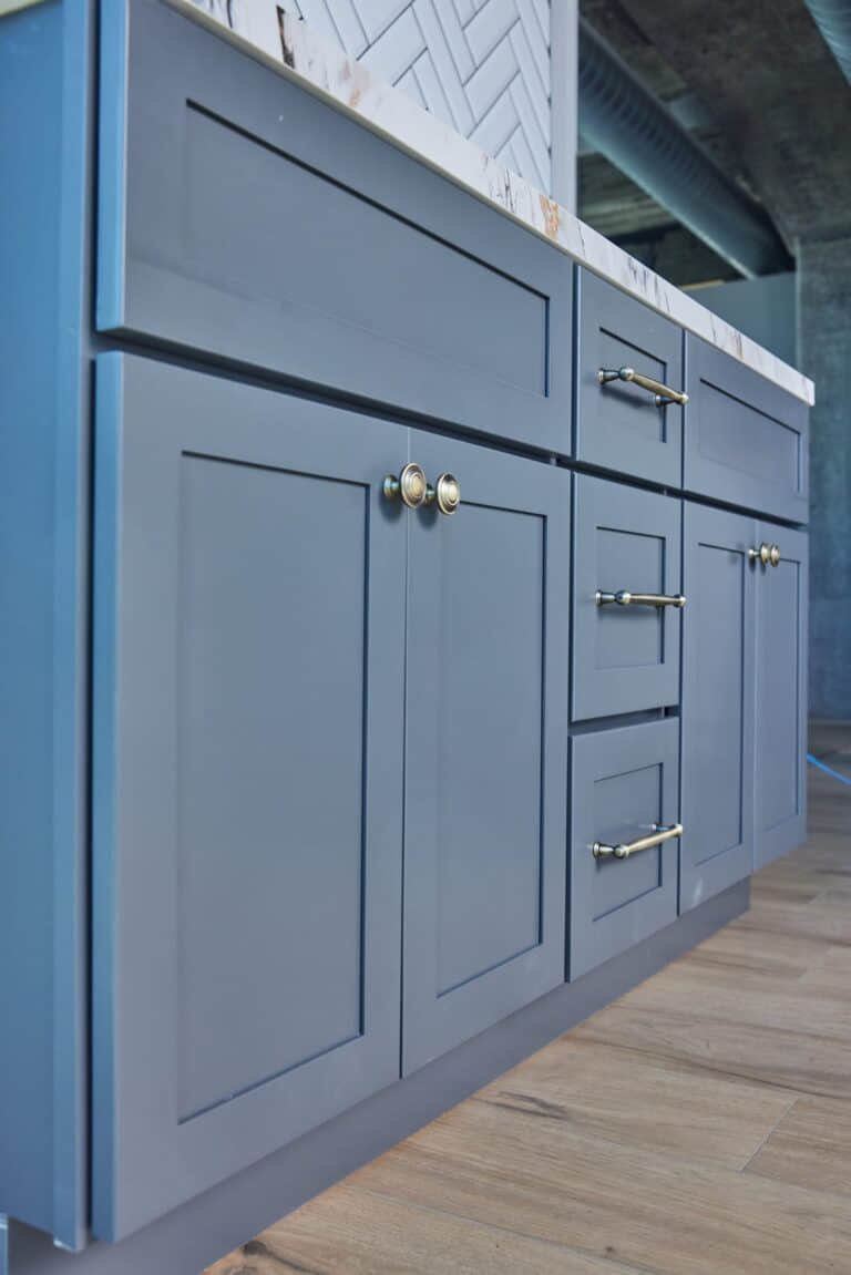 Blue kitchen cabinets with brass handles on wooden floor.