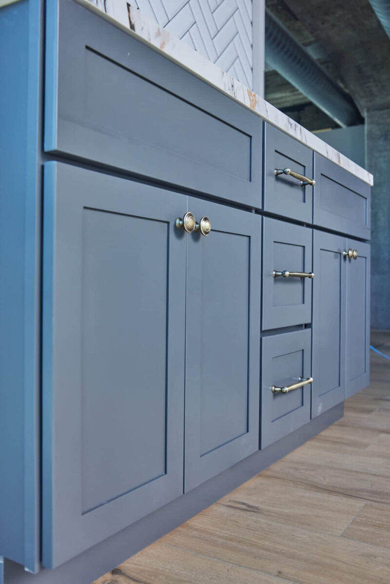 Blue kitchen cabinets with brass handles on wooden floor.