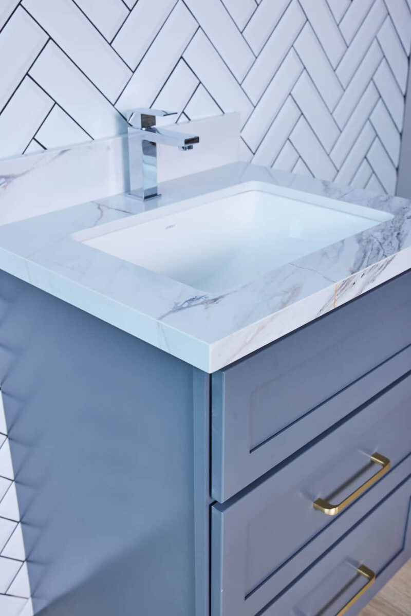 Modern bathroom vanity with marble countertop and herringbone tile backsplash.