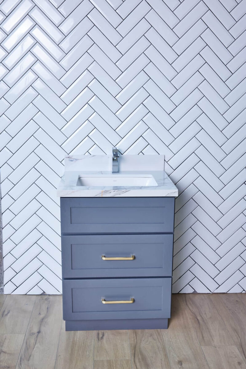 Gray bathroom vanity with herringbone tile backsplash.