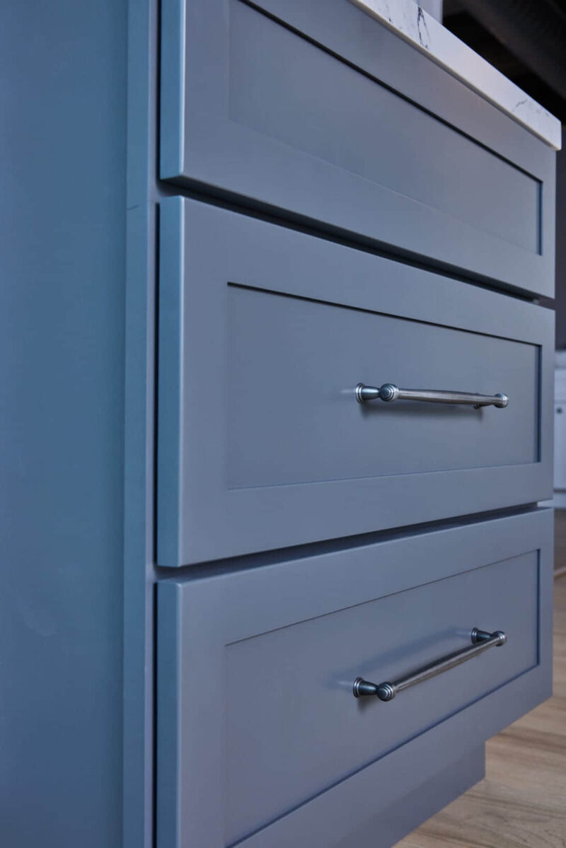Blue kitchen cabinets with silver handles and marble countertop.
