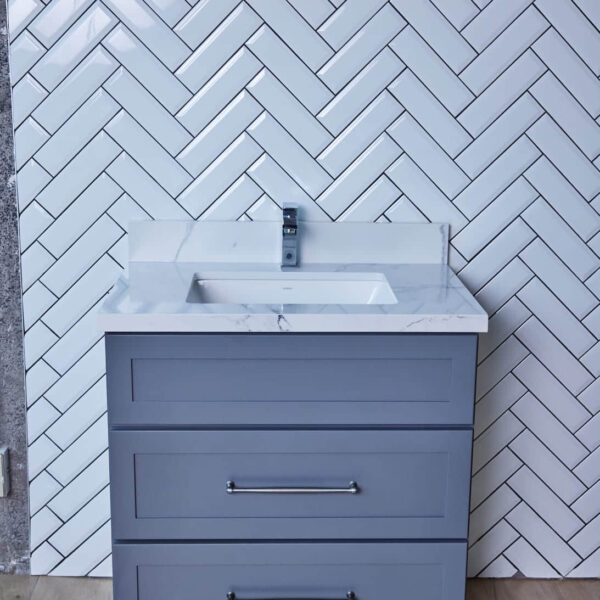 Gray bathroom vanity with white sink against herringbone tile wall.