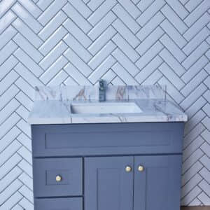 Gray bathroom vanity with marble countertop against herringbone tile wall.
